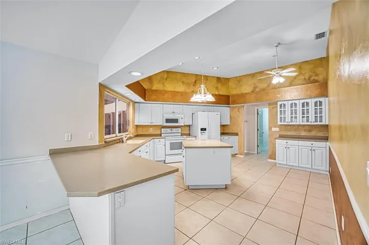Kitchen with a kitchen island, white appliances, decorative light fixtures, light tile patterned floors, and a peninsula