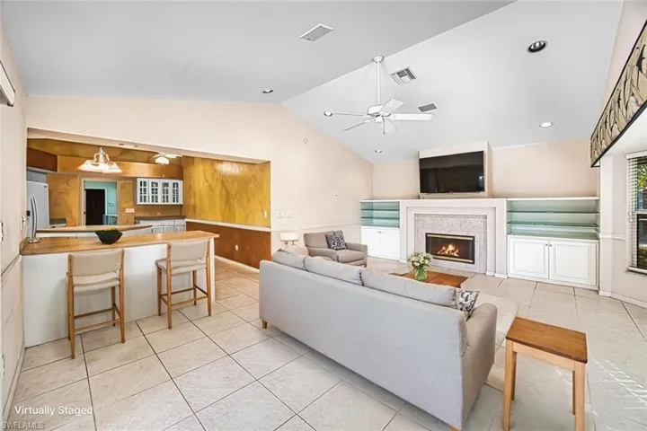 *VIRTUALLY STAGED* Living area featuring light tile patterned floors, vaulted ceiling, ceiling fan, a warm lit fireplace, and recessed lighting