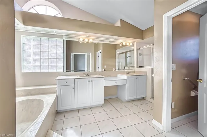 Bathroom featuring lofted ceiling, double vanity, a shower stall, light tile patterned floors, and a garden tub