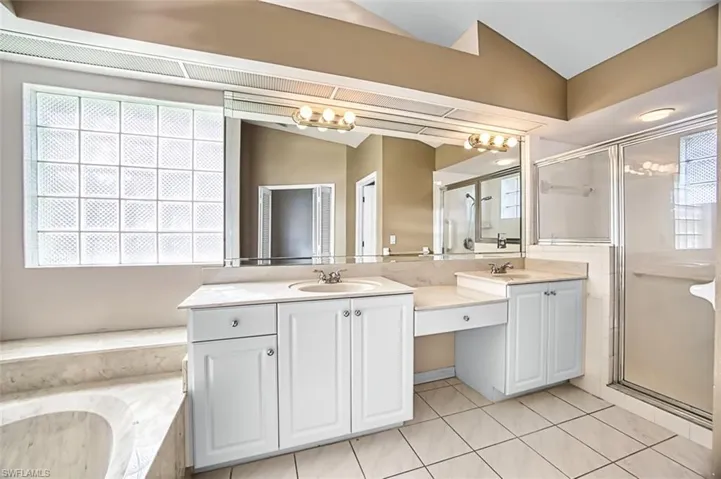 Full bathroom featuring double vanity, a shower stall, lofted ceiling, a tub with marble appearance, and light tile patterned floors