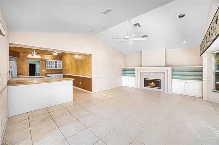 Unfurnished living room with a ceiling fan, lofted ceiling, light tile patterned floors, a warm lit fireplace, and recessed lighting