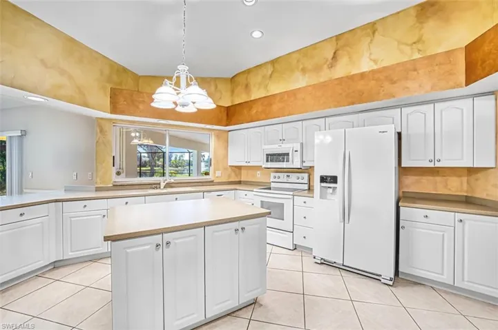 Kitchen with white cabinetry, white appliances, decorative light fixtures, light countertops, and a chandelier