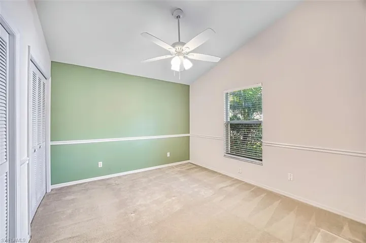 Unfurnished bedroom featuring two closets, vaulted ceiling, carpet flooring, and ceiling fan