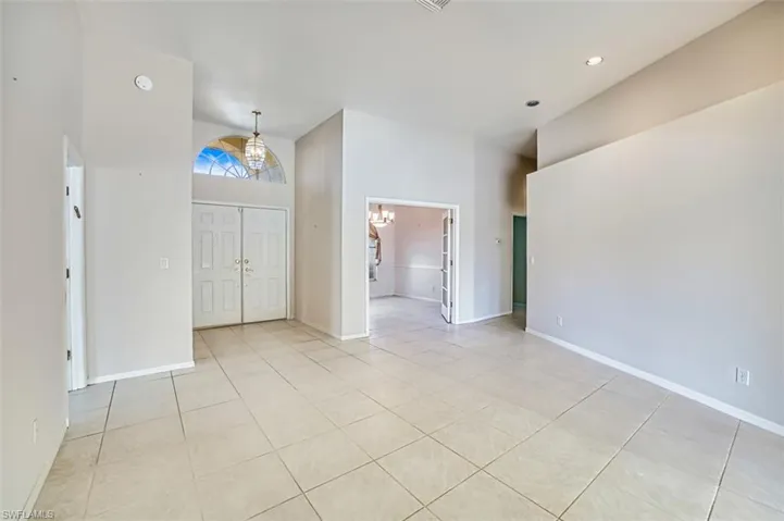 Empty room with high vaulted ceiling, a chandelier, light tile patterned floors, and recessed lighting