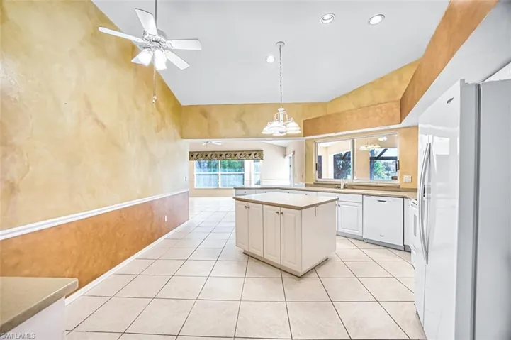 Kitchen with white appliances, white cabinetry, vaulted ceiling, light countertops, and light tile patterned floors