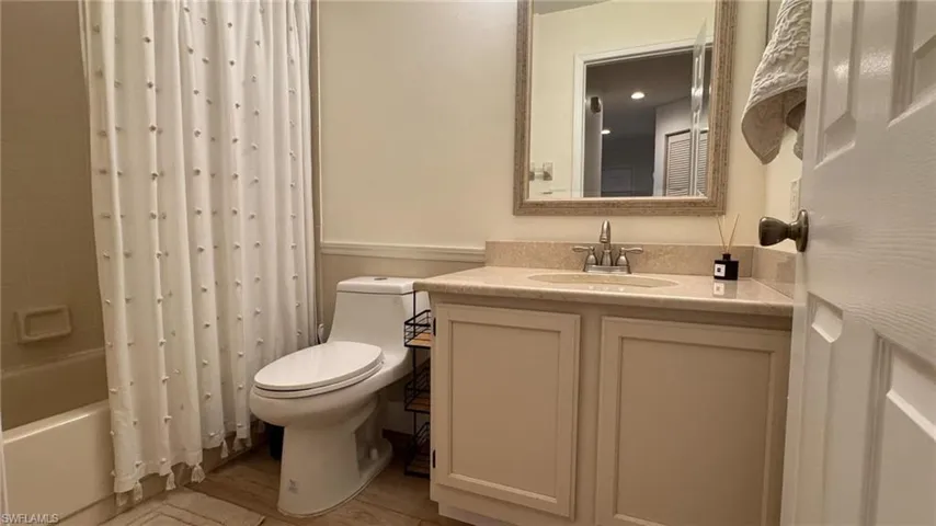 Full guest bathroom with shower / bath combo with shower curtain, vanity, wood-type flooring, and toilet
