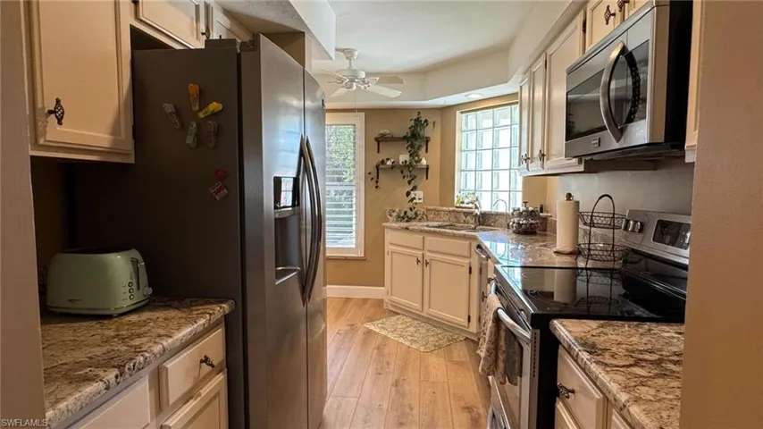 Kitchen with light wood-type flooring, light stone counters, stainless steel appliances, ceiling fan, and sink