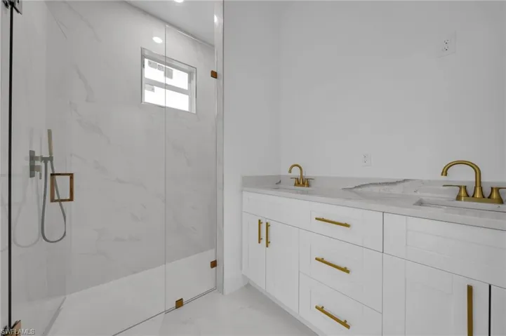Bathroom featuring double vanity, light marble finish floors, and a marble finish shower