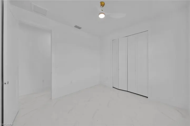 Unfurnished bedroom featuring light marble finish flooring, a ceiling fan, and a closet