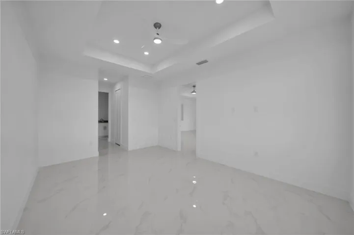 Empty room featuring a tray ceiling, recessed lighting, light marble finish flooring, and a ceiling fan