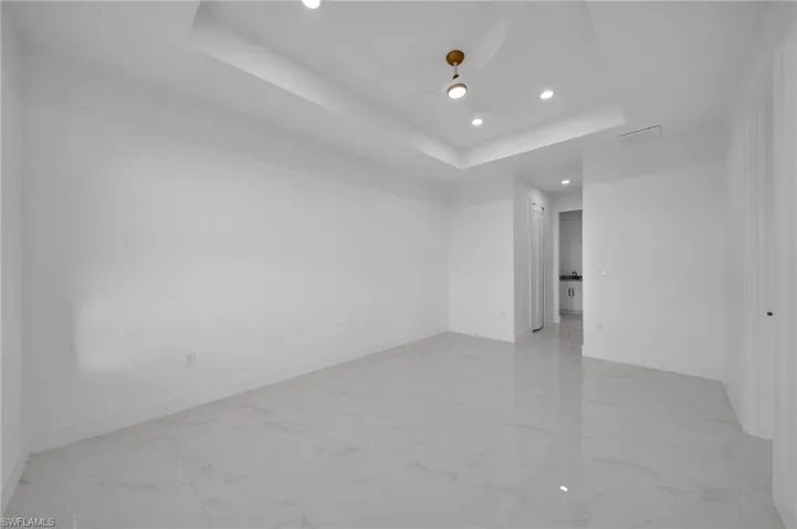 Unfurnished room featuring recessed lighting, a tray ceiling, light marble finish flooring, and a ceiling fan