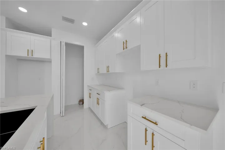 Kitchen featuring light marble finish floors, light stone counters, white cabinetry, and recessed lighting