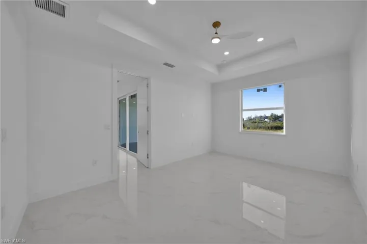Empty room featuring a raised ceiling, recessed lighting, light marble finish floors, and a ceiling fan