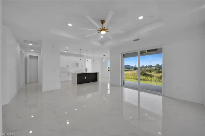 Unfurnished living room with a raised ceiling, recessed lighting, light marble finish floors, and a ceiling fan