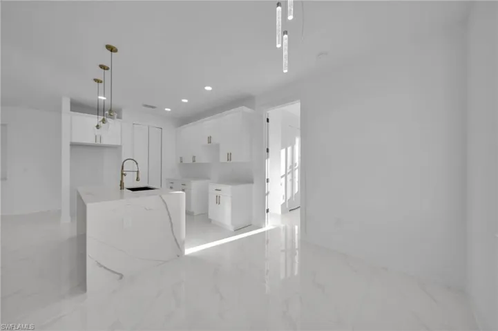 Kitchen featuring white cabinetry, a kitchen island with sink, decorative light fixtures, recessed lighting, and light marble finish floors