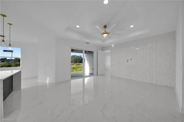 Unfurnished room featuring light marble finish flooring, a tray ceiling, recessed lighting, an accent wall, and a ceiling fan
