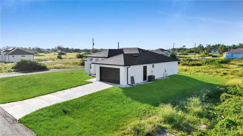 View of side of home featuring roof with shingles, stucco siding, driveway, and a yard