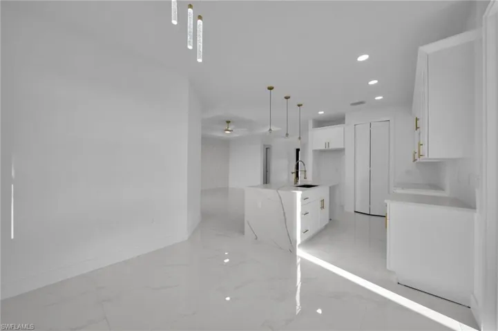 Kitchen featuring white cabinets, recessed lighting, light stone counters, decorative light fixtures, and light marble finish flooring