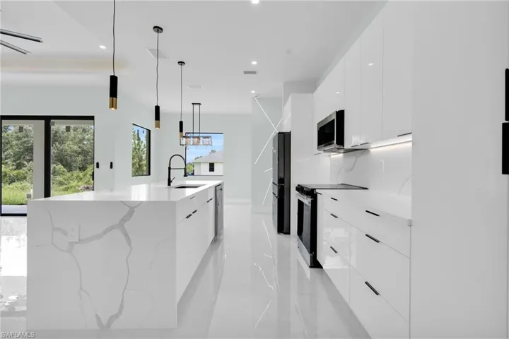 Kitchen with modern cabinets, appliances with stainless steel finishes, white cabinets, a large island with sink, and recessed lighting