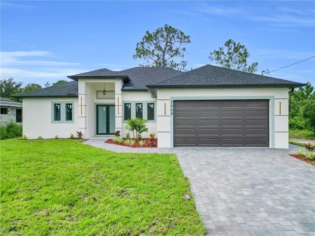 View of front of house featuring stucco siding, decorative driveway, a front lawn, and an attached garage