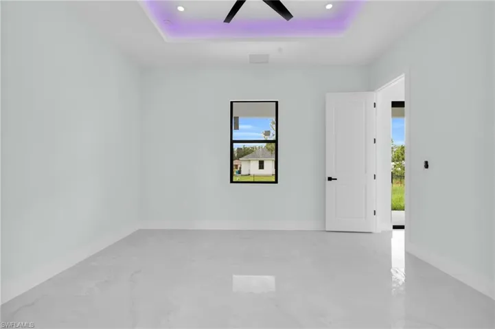 Empty room with a raised ceiling, plenty of natural light, marble finish flooring, a ceiling fan, and recessed lighting