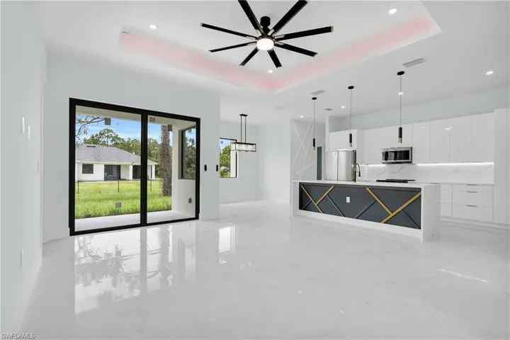 Unfurnished living room featuring a tray ceiling, recessed lighting, ceiling fan, and light marble finish floors