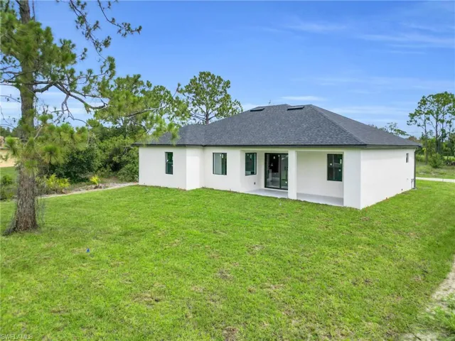 Back of house featuring stucco siding, roof with shingles, a lawn, and a patio area