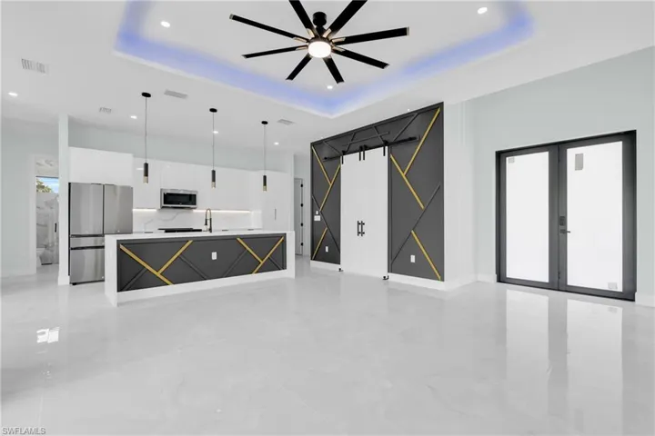 Unfurnished living room with a raised ceiling, a ceiling fan, light marble finish flooring, recessed lighting, and french doors