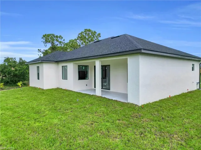 Rear view of house with a patio, stucco siding, a yard, and a shingled roof