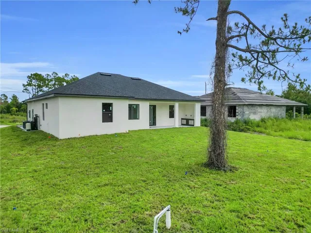 Rear view of property with stucco siding, a yard, and a shingled roof