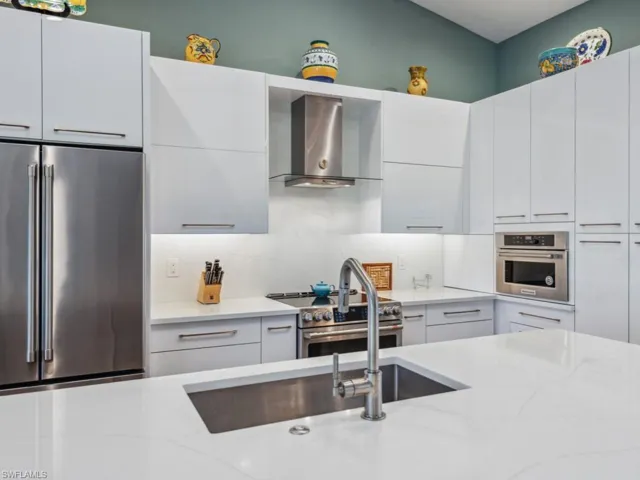 Kitchen featuring light stone countertops, wall chimney exhaust hood, premium appliances, backsplash, and white cabinets