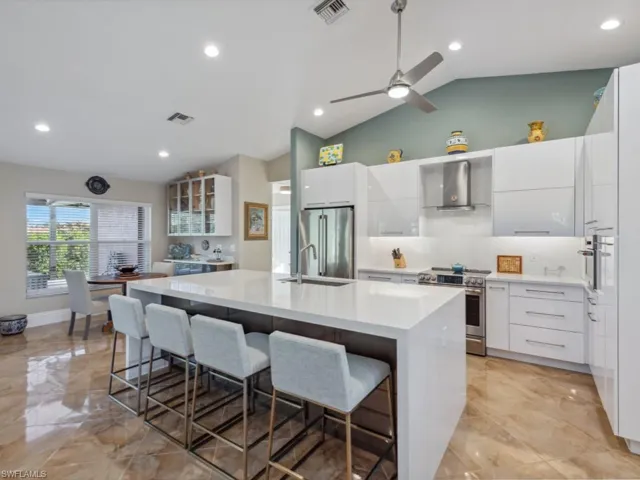 Kitchen with lofted ceiling, a center island with sink, white cabinets, appliances with stainless steel finishes, and a breakfast bar area
