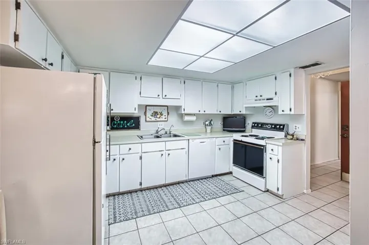 Kitchen with white appliances, light countertops, white cabinetry, light tile patterned flooring, and under cabinet range hood