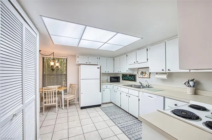 Kitchen featuring light countertops, white appliances, white cabinetry, light tile patterned flooring,