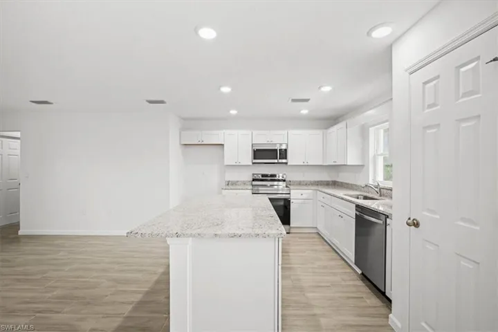 Kitchen featuring a kitchen island, white cabinets, stainless steel appliances, wood finish floors, and light stone counters
