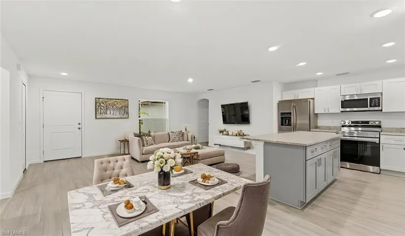 Kitchen with stainless steel appliances, open floor plan, a kitchen island, light stone countertops, and a breakfast bar