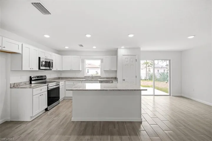 Kitchen with stainless steel appliances, light stone counters, wood finish floors, white cabinets, and recessed lighting