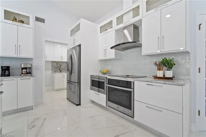 Kitchen featuring appliances with stainless steel finishes, wall chimney exhaust hood, white cabinetry, and decorative backsplash