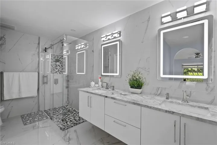 Bathroom with marble tiled floors, double vanity, a marble finish shower, and ceiling fan