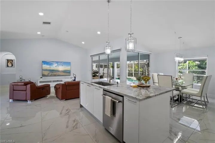 Kitchen featuring dishwasher, vaulted ceiling, modern cabinets, white cabinetry, and light marble finish flooring