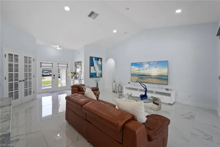 Living area with light marble finish floors, french doors, vaulted ceiling, and recessed lighting
