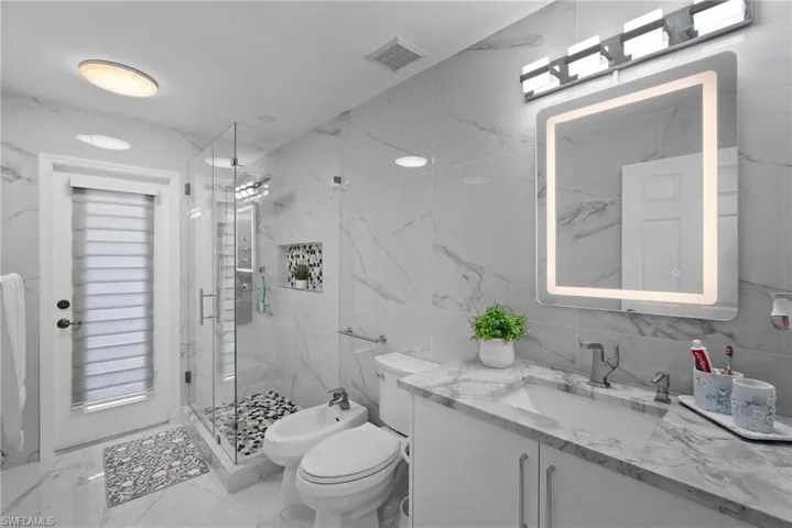 Bathroom with vanity, marble look tile flooring, a bidet, a marble finish shower, and tile walls