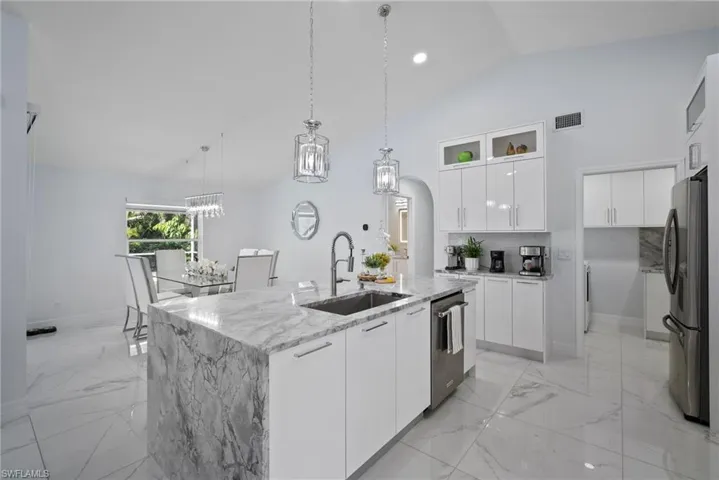 Kitchen featuring stainless steel appliances, modern cabinets, light stone countertops, light marble finish floors, and high vaulted ceiling