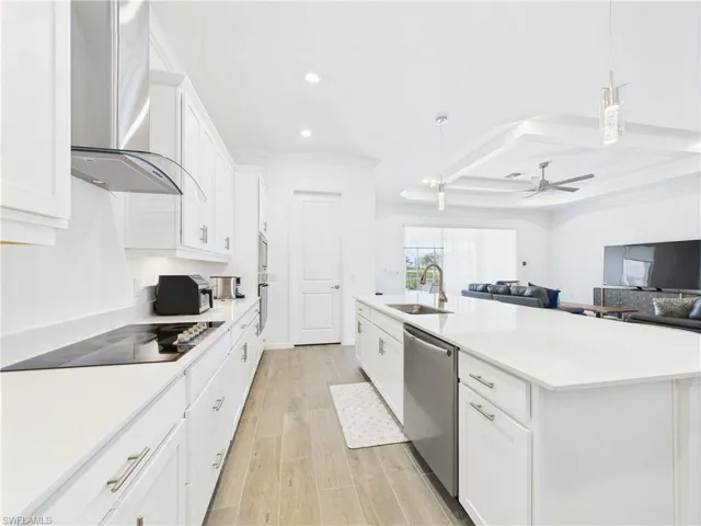 Kitchen featuring pendant lighting, white cabinets, open floor plan, wall chimney range hood, and recessed lighting