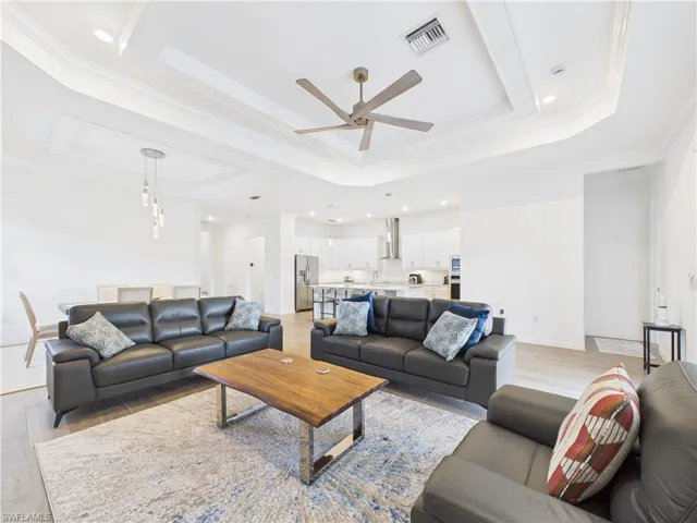 Living area featuring a raised ceiling, crown molding, ceiling fan, light wood finished floors, and recessed lighting