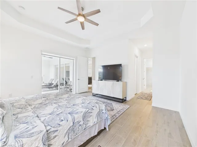 Bedroom with a raised ceiling, light wood-style floors, a ceiling fan, and ensuite bathroom