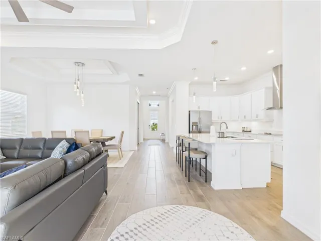 Living area with a raised ceiling, recessed lighting, light wood-style floors, crown molding, and ceiling fan