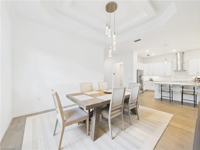 Dining space with ornamental molding, a raised ceiling, and light wood-style flooring