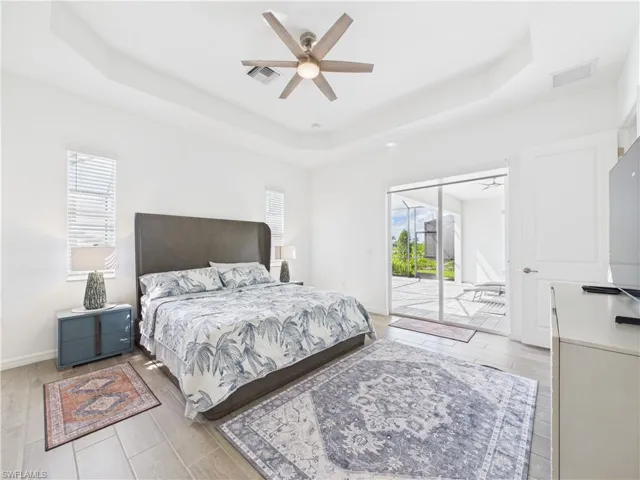 Bedroom featuring a raised ceiling, access to exterior, light wood-type flooring, and ceiling fan