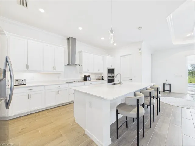 Kitchen featuring wood tiled floors, a kitchen breakfast bar, hanging light fixtures, crown molding, and white cabinets